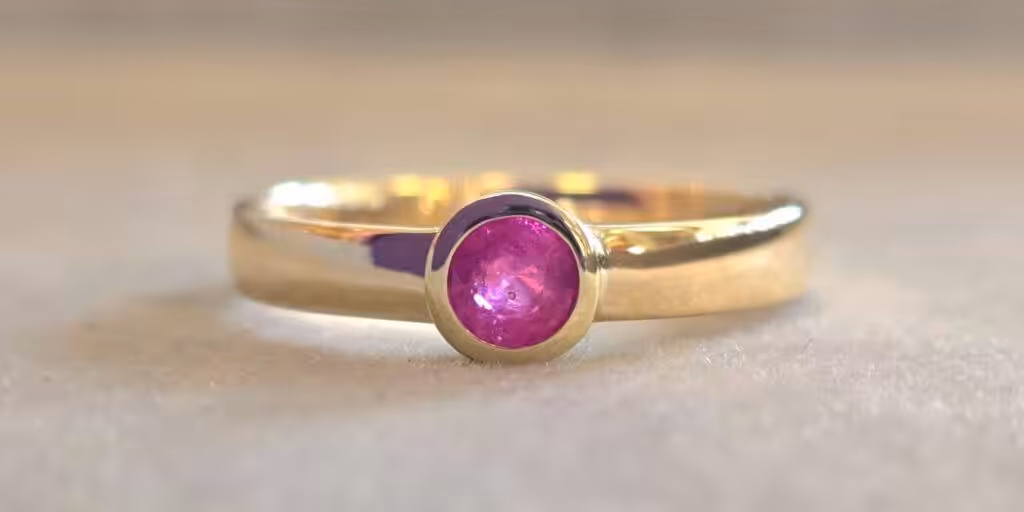 Trauringe selber schmieden: Personalisierte Goldringe mit pinkem Edelstein.