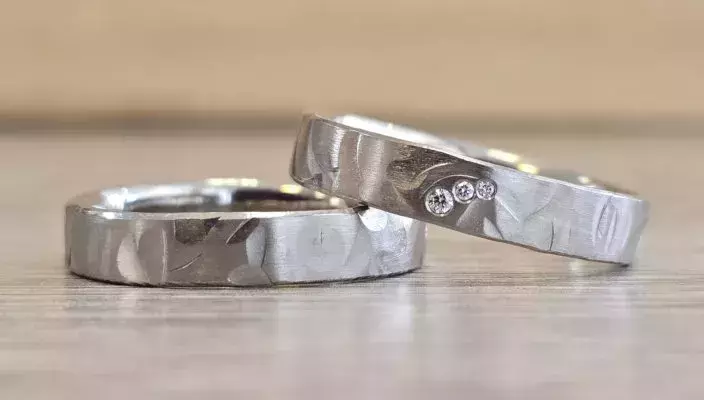 Selbstgeschmiedete Trauringe aus Weißgold mit strukturierter Oberfläche und drei Brillanten, gefertigt von einem Paar im Trauringkurs.