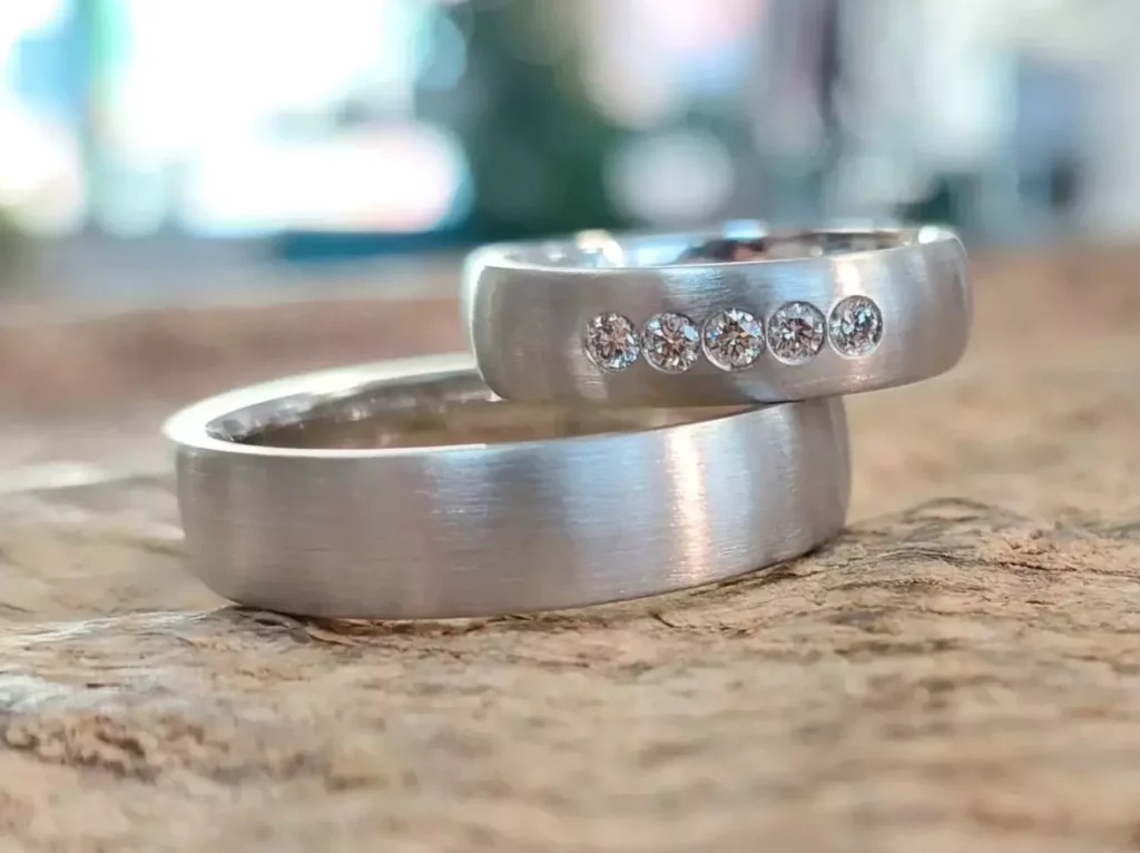 Selbst geschmiedete Trauringe aus Weißgold, einer davon mit fünf Diamanten, aus einem Trauringkurs der Schmuckwerkstatt Trolese.