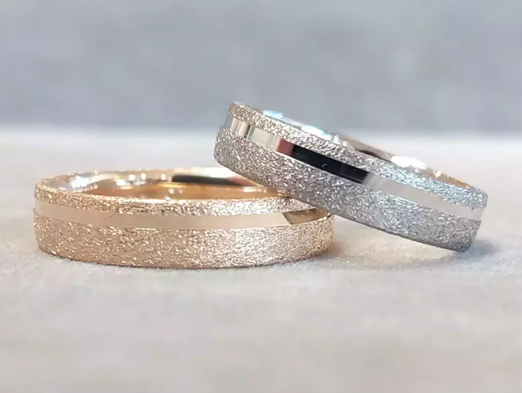 Selbstgeschmiedete Trauringe aus Roségold und Weißgold mit strukturierter Oberfläche und glänzender Mittelspur aus der Schmuckwerkstatt Trolese.