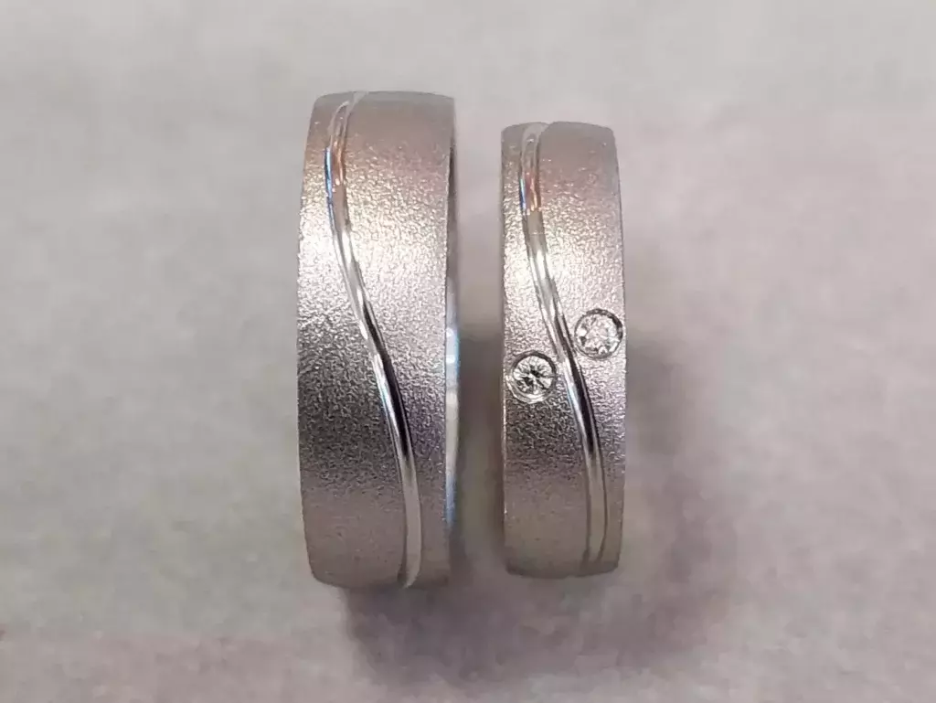 Selbstgeschmiedete Trauringe aus Weißgold mit strukturierter Oberfläche, geschwungener Glanzlinie und zwei Brillanten aus dem Trauringkurs der Schmuckwerkstatt Trolese.