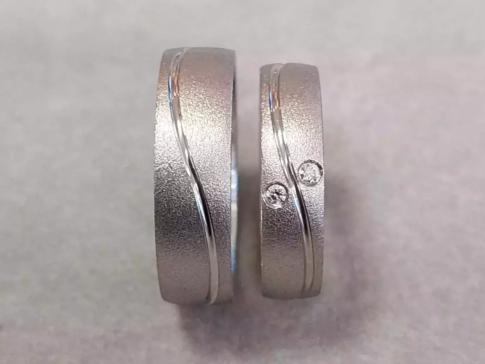 Selbstgeschmiedete Trauringe aus Weißgold mit strukturierter Oberfläche, geschwungener Glanzlinie und zwei Brillanten aus dem Trauringkurs der Schmuckwerkstatt Trolese.