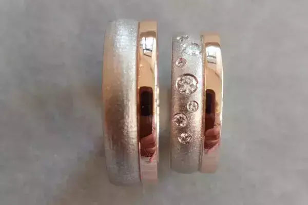 Bicolor-Trauringe aus Silber und Roségold mit strukturierter Oberfläche und mehreren Brillanten.