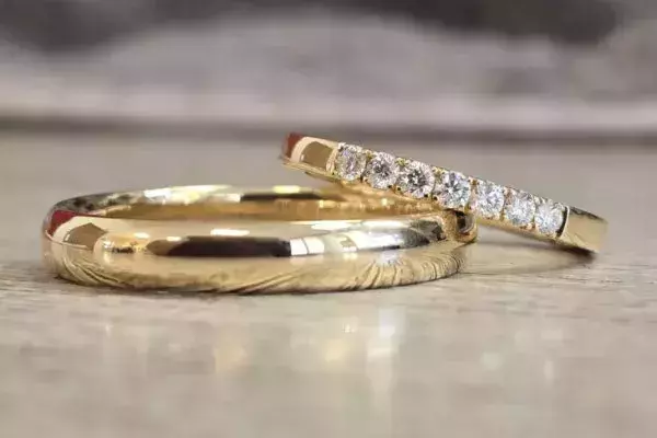 Polierte Trauringe aus Gelbgold, einer davon mit einer Reihe funkelnder Brillanten.
