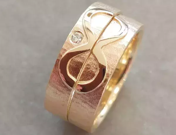 Zwei selbst geschmiedete Trauringe aus Gold mit Unendlichkeitssymbol und Brillant.