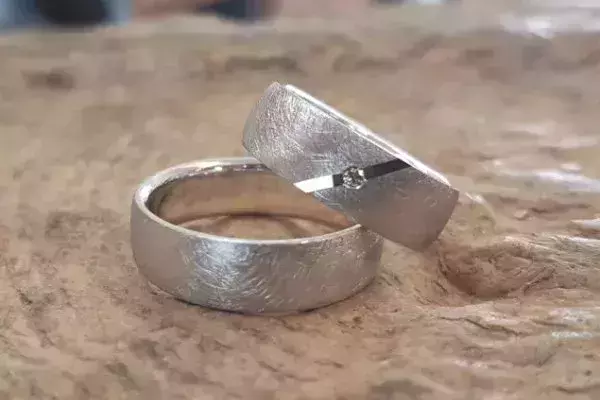 Von Kursteilnehmern selbst geschmiedete Trauringe aus Weißgold mit matter Oberfläche und kleinem Brillant.