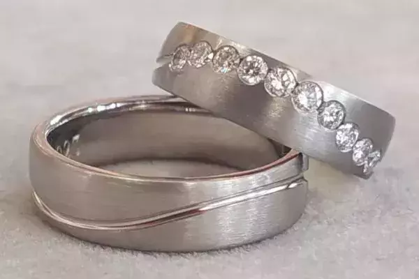 Von Kursteilnehmern selbst geschmiedete Trauringe aus Weißgold mit geschwungener Linie und mehreren Brillanten.