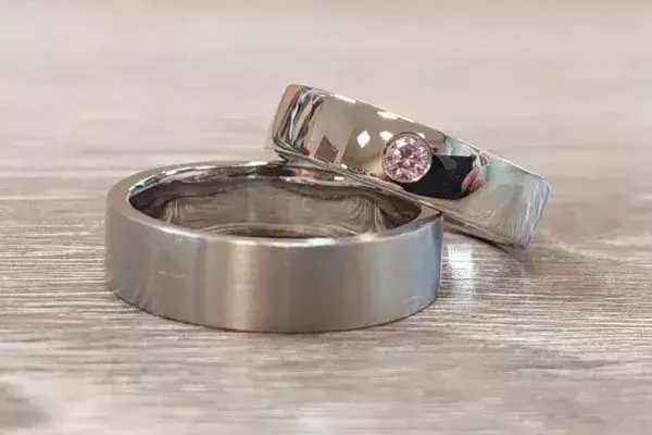 Zwei Trauringe aus Weißgold, einer mattiert und einer poliert mit rosafarbenem Edelstein.