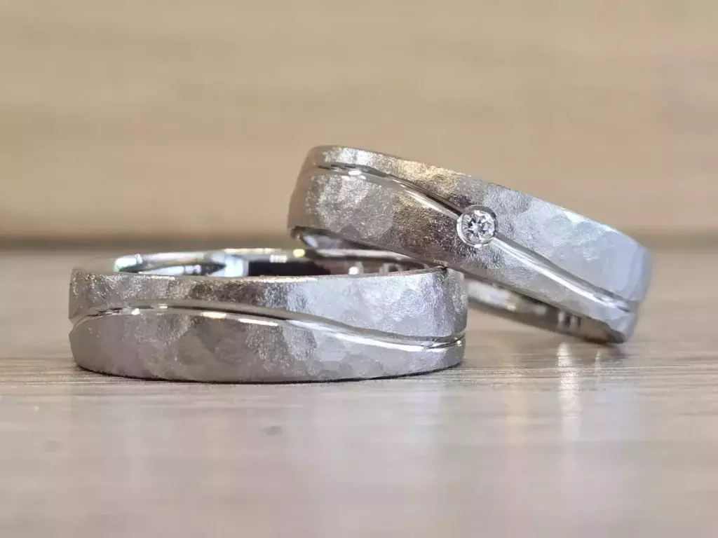 Selbst geschmiedete Trauringe mit strukturierter matter Oberfläche, geschwungener Linie und Diamant