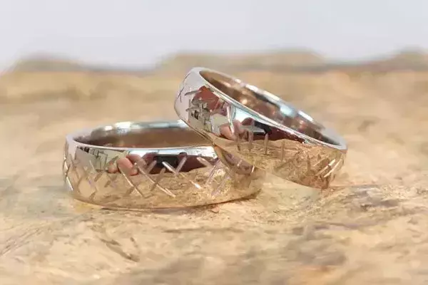 Zwei selbst geschmiedete Trauringe mit geometrischem Kreuzmuster auf einer Holzoberfläche.
