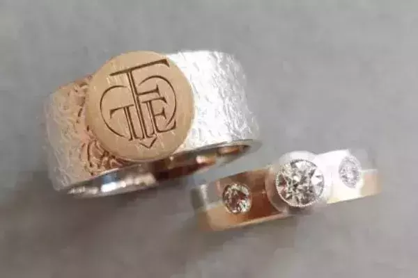 Zwei selbst geschmiedete Trauringe aus Weißgold und Roségold mit Monogramm, strukturierter Oberfläche und drei Brillanten.