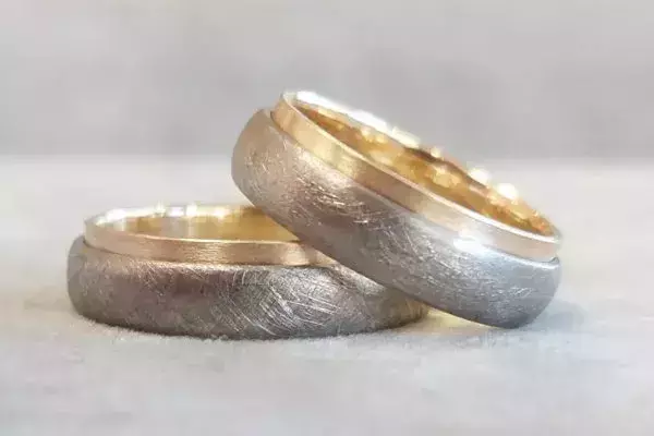 Zwei selbst geschmiedete Trauringe aus Weißgold und Gelbgold mit matter, strukturierter Oberfläche.