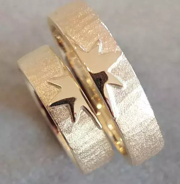 Selbst geschmiedete Trauringe aus Gold mit matter Oberfläche und glänzendem Sternmotiv.